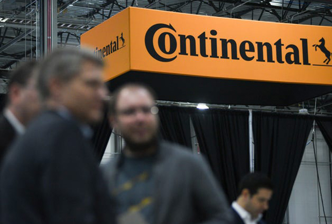 Four blurry men pictured in foreground with an in focus display of the Continental logo behind them