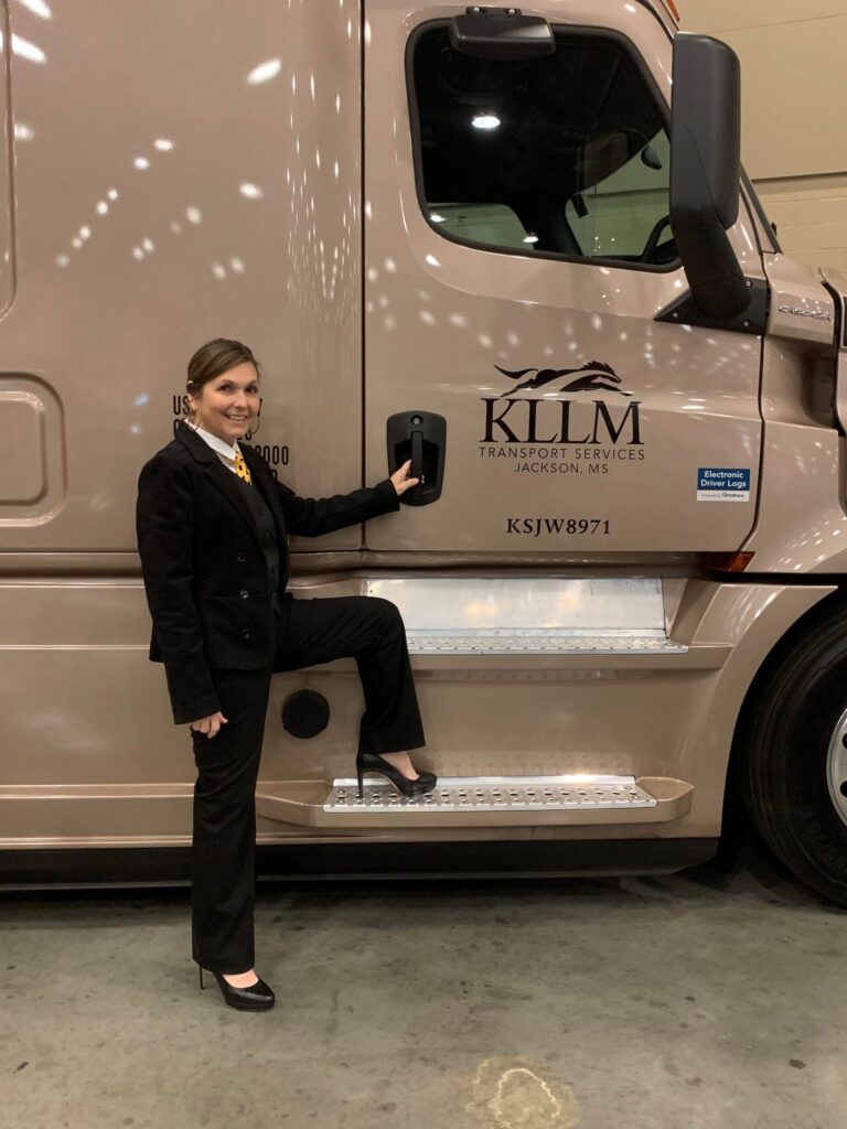 Woman in business suit posing with semi truck with KLLM Transport Services logo