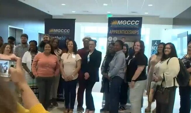 Group of men and women being photographed in front of MGCCC Apprenticeships signs