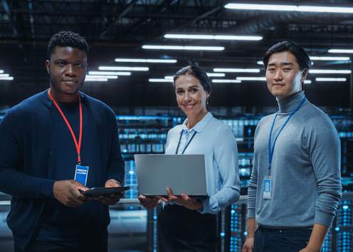 Diverse Team of Data Center System Administrators and IT Specialists Use Laptop and Tablet Computers, Smiling on Camera. IT Engineers work on Cyber Security Protection in Cloud Computing Server Farm.