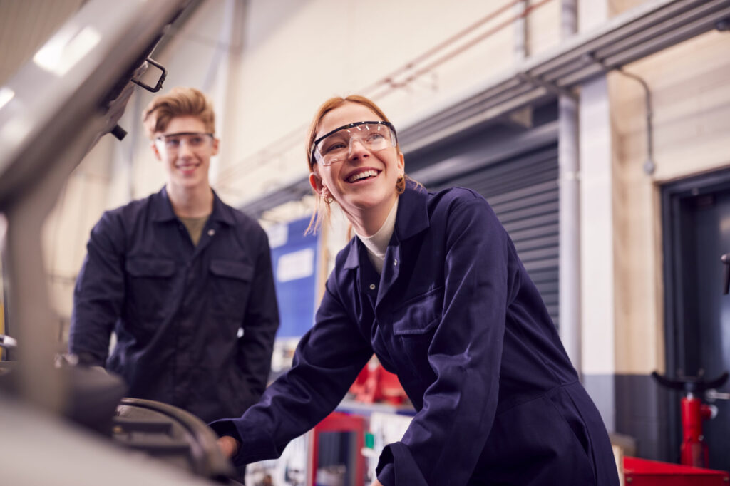 Male and female students looking at car engine on auto mechanic apprenticeship course at college